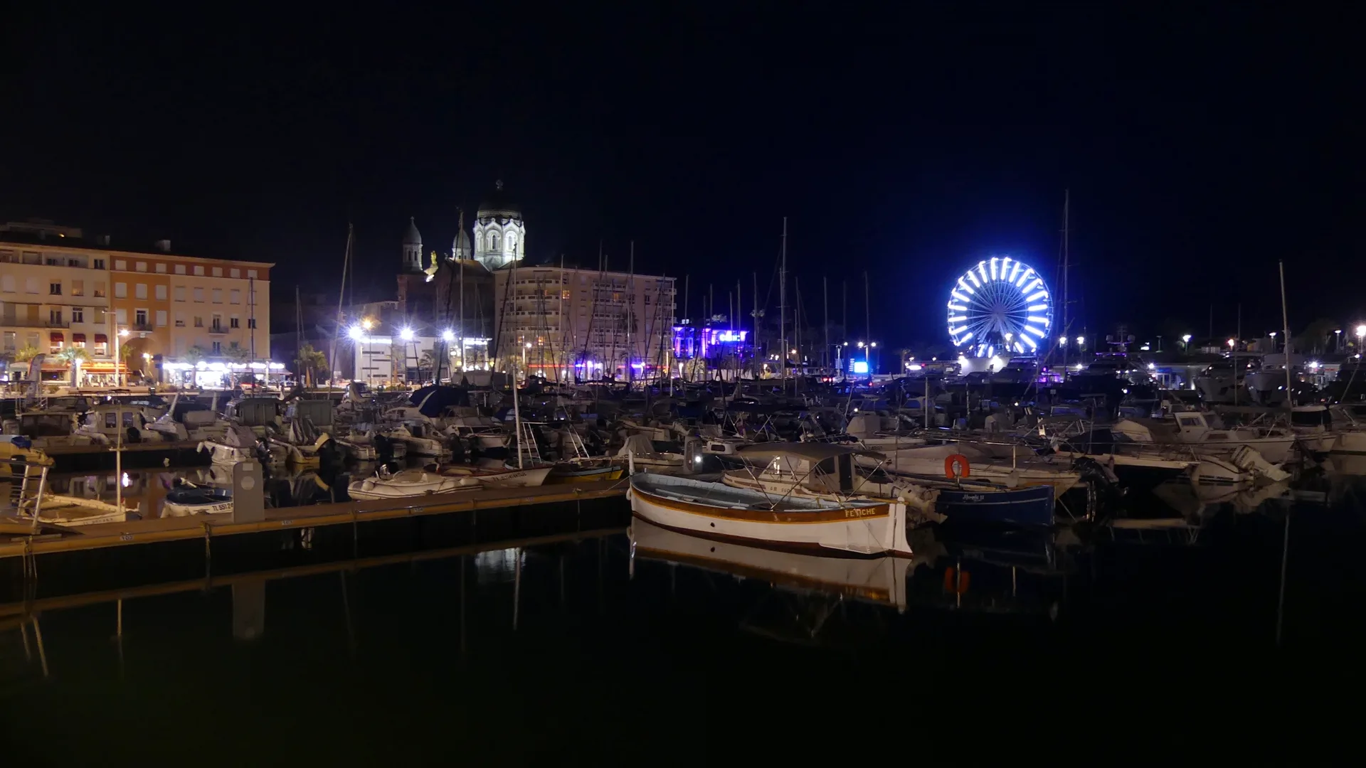 Le port de Saint-Raphaël la nuit : basilique illuminée, grande roue et terrasses éclairées au bord de l'eau